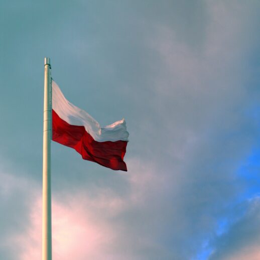 flaga Polski powiewająca na maszcie na tle nieba