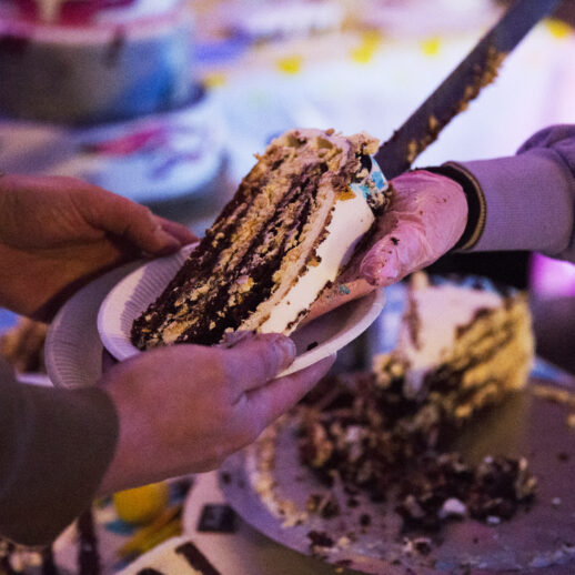 dłonie kobiety krojącej tort i przekazującej jego kawałek drugiej osobie na talerz