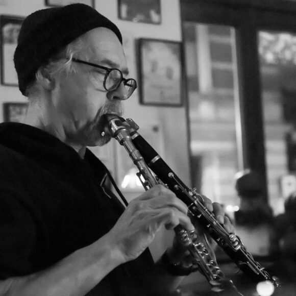 Jerzy Mazzol w czarno-białych kolorach. Stoi bokiem i gra na instrumencie dętym.