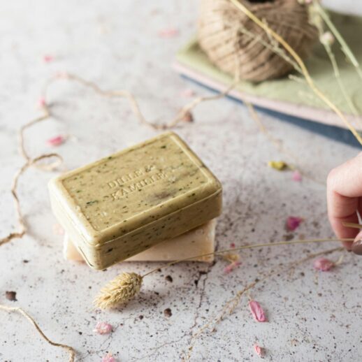 Dwa mydła, jedno zielone a pod nim beżowe. Wokół nich gałązki.