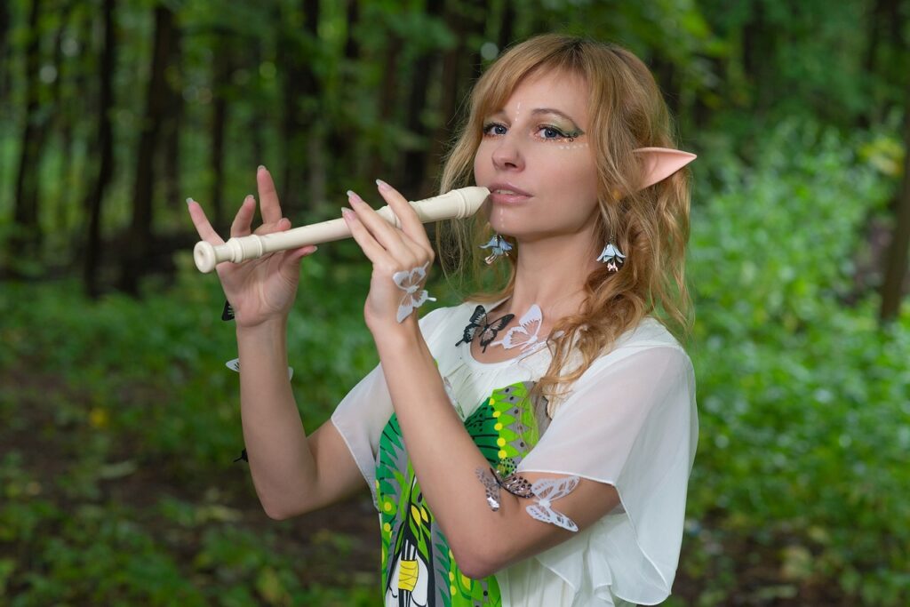 Blondwłosa dziewczyna z długimi uszami, jak u elf. Ma przyklejone do skóry białe i czarne motylki. Stoi w lesie i gra na flecie.