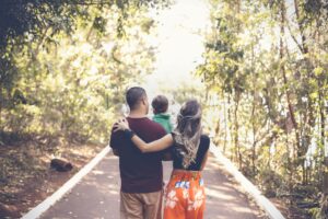 Zdjęcie przedstawiające młodą parę rodziców idącą przez park z dzieckiem.