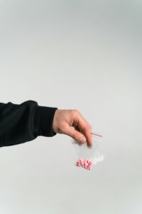 Zdjęcie przedstawiające dłoń trzymającą dwie saszetki z tabletkami - różowymi i białymi.